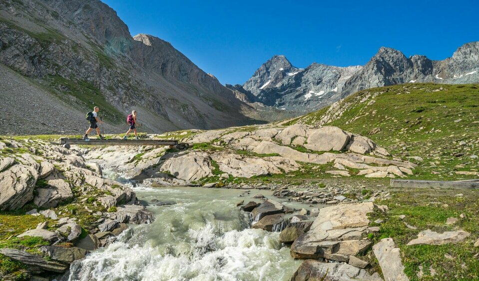 Weitwanderer überqueren Bach im oberen Leitertal mit Blick auf den Großglockner, Etappe 4 der Glocknerkrone in Osttirol.
