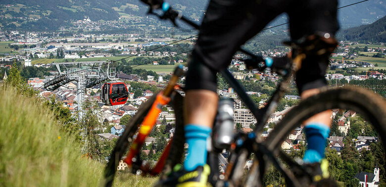Nahaufnahme eines Radlfahrers auf dem Alban Lakata Trail im Bikepark Lienz, mit Blick auf die Lienzer Bergbahn und die Stadt.
