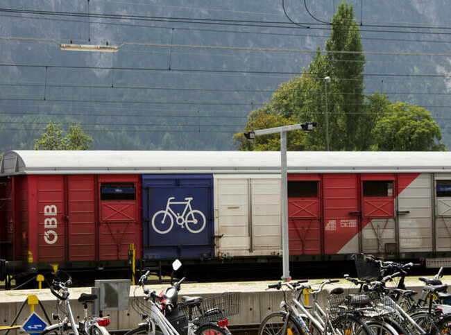 ÖBB Radtransport Wagon. Im Vordergrund sind Fahrräder und ein Moped an Fahrradständern abgestellt.