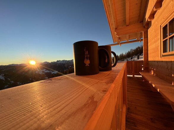 Ein einfaches Holzgeländer mit zwei Tassen, während die Sonne am Horizont aufgeht.