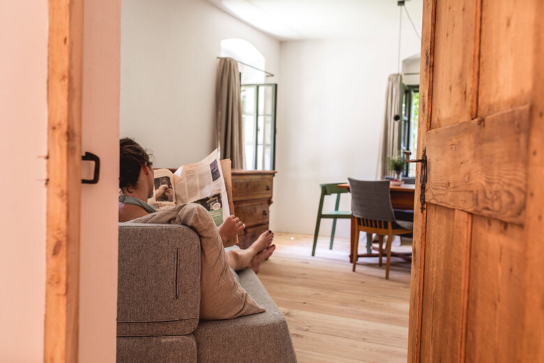 Eine Frau entspannt in ihrer Unterkunft auf einem Sofa und liest Zeitung.