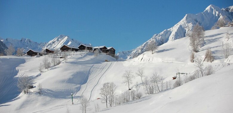 Das schneebedeckte Skigebiet Bichllift. Blick auf einen Skilift und mehrere Gebäude auf einem Hügel.