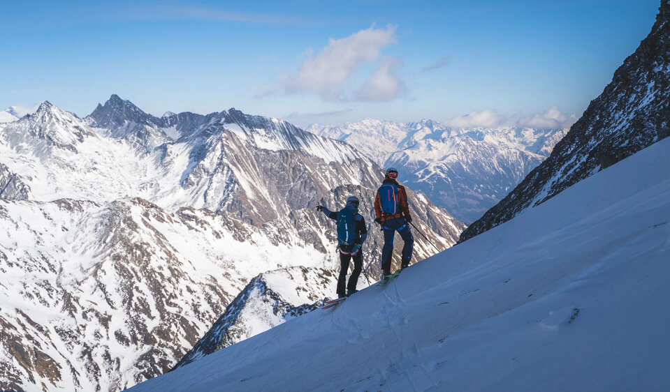Zwei Skitourengeher:innen genießen den Ausblick aufs Regentörl und blicken in die verschneite Berglandschaft.
