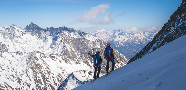 Zwei Skitourengeher:innen genießen den Ausblick aufs Regentörl und blicken in die verschneite Berglandschaft.