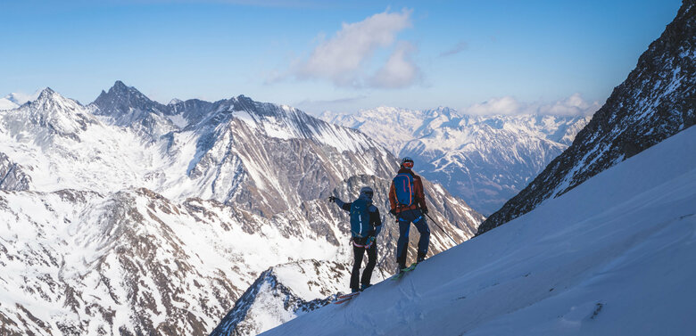 Zwei Skitourengeher:innen genießen den Ausblick aufs Regentörl und blicken in die verschneite Berglandschaft.