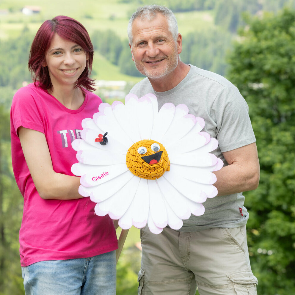Unser Familiennestteam Engelbert und Sarah halten zusammen Gisela Gänseblümchen in der Hand.