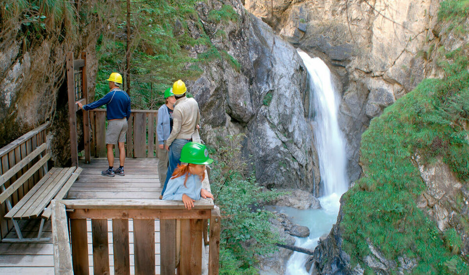 Vier Personen stehen fasziniert auf der Aussichtskanzel des Wasserschaupfades und beobachten das tosend herabschießende Wasser in der Schlucht.