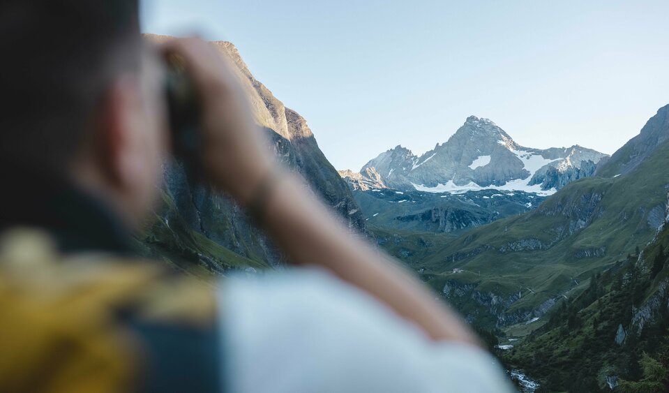 Nationalpark-Ranger blickt durch ein Fernglas auf den weit entfernten Großglockner.
