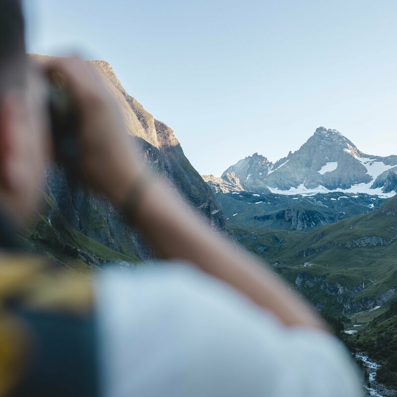 Nationalpark-Ranger blickt durch ein Fernglas auf den weit entfernten Großglockner.
