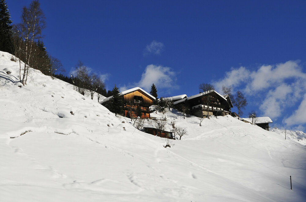 Ein verschneiter Bergbauernhof liegt auf einer Anhöhe im sonnigen St. Veit im Defereggen.