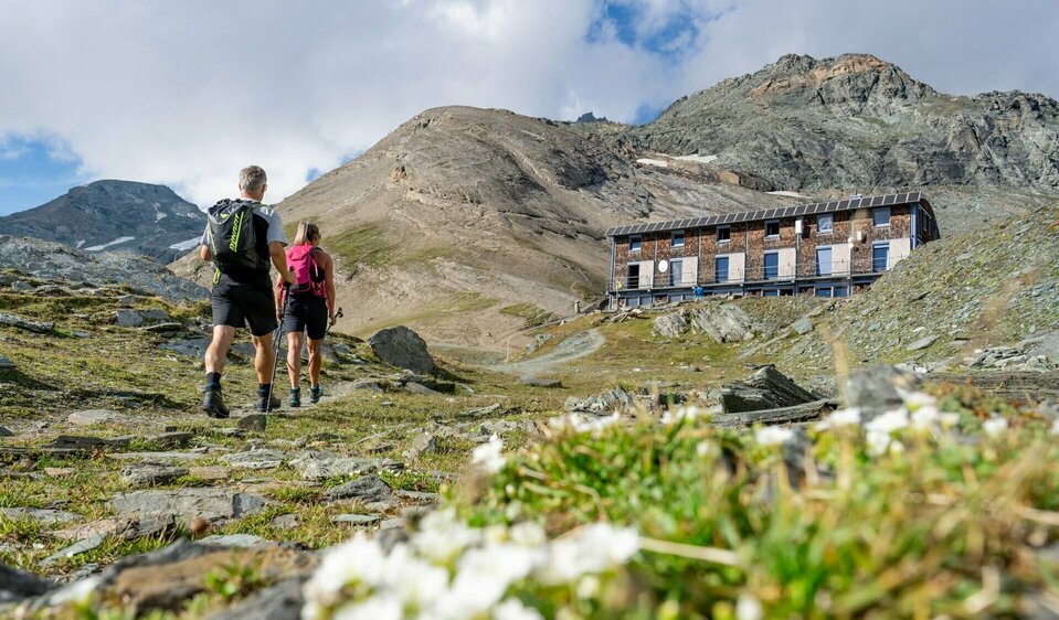 Wanderer auf Etappe 3 der Glocknerkrone in Osttirol nahe Kals am Großglockner mit Blick auf Schutzhütte und Gebirge beim Weitwandern.