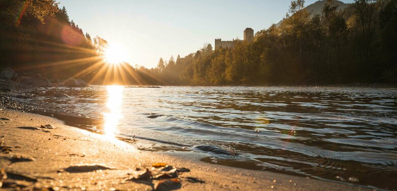 Das Ufer der Isel in der untergehenden Sonne. Im Hintergrund Blick auf das Schloss Bruck.