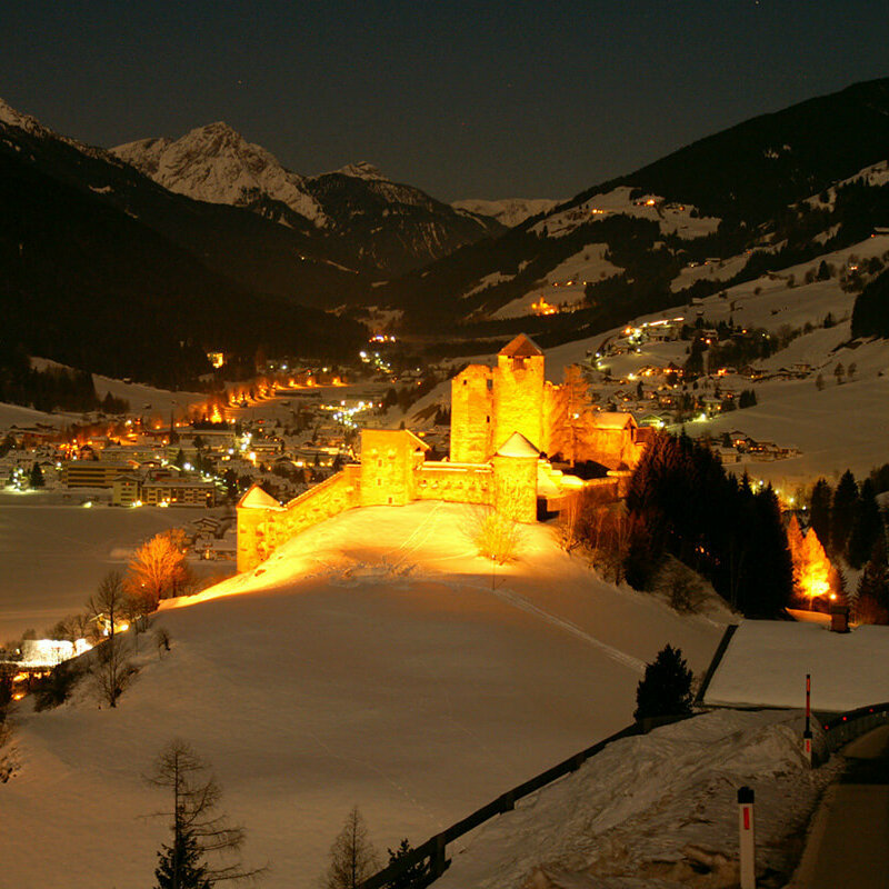 Beleuchtete Burg Heinfels bei Nacht im Winter von Schnee bedeckt.