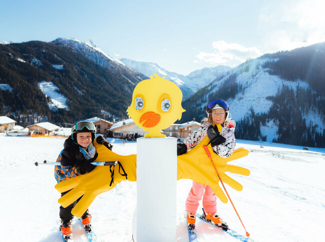 Zwei Kinder stehen an einer farbenfrohen Entenfigur im Kinderland in Obertilliach