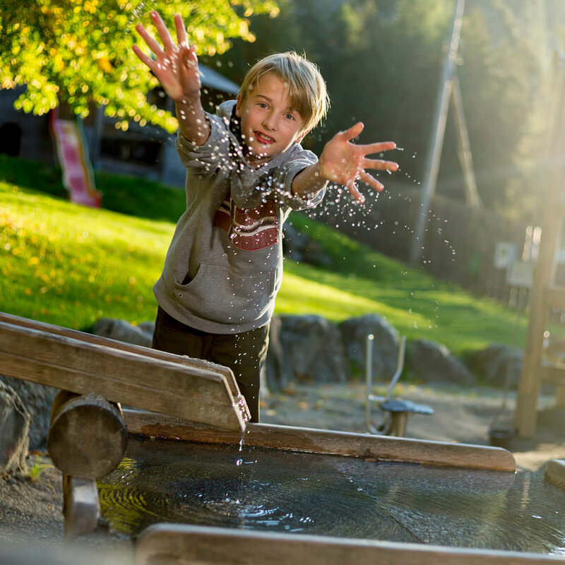Auf dem Bild ist ein Kind zu sehen, das am Spielplatz der Galitzenklamm etwas Wasser in Richtung des Fotografen spritzt.