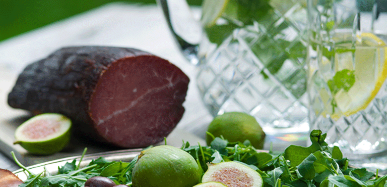 Henkele in feine Scheiben aufgeschnitten und auf einer runden Platte angerichtet mit Feigen, Oliven und Rucola.