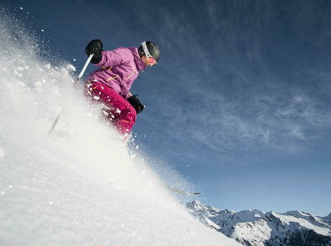 Eine pink-lila gekleidete Freeriderinn im Pulverschnee im Großglockner Resort in Kals-Matrei.