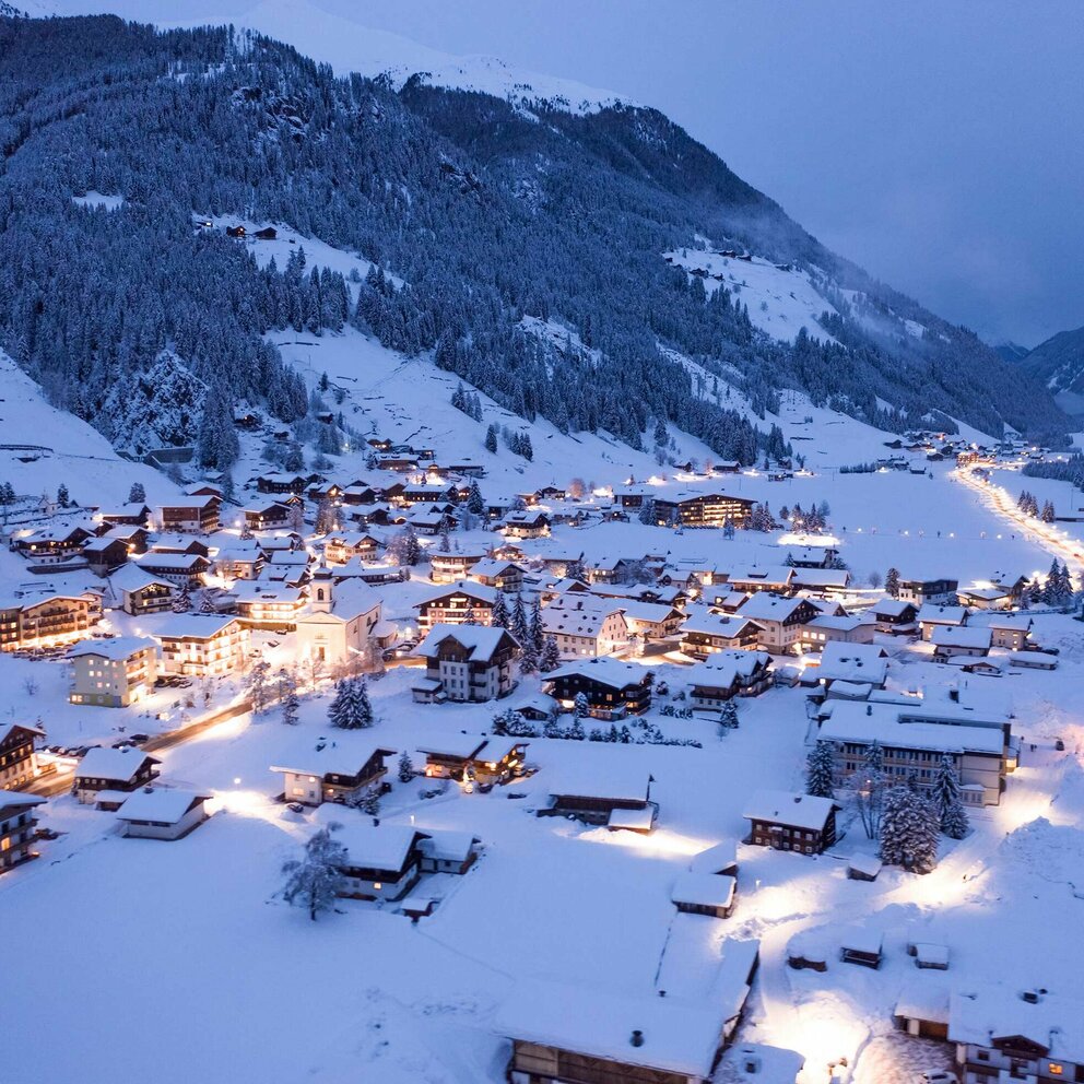 Blick auf das winterliche, beleuchtete St. Jakob im Defereggental am Abend.