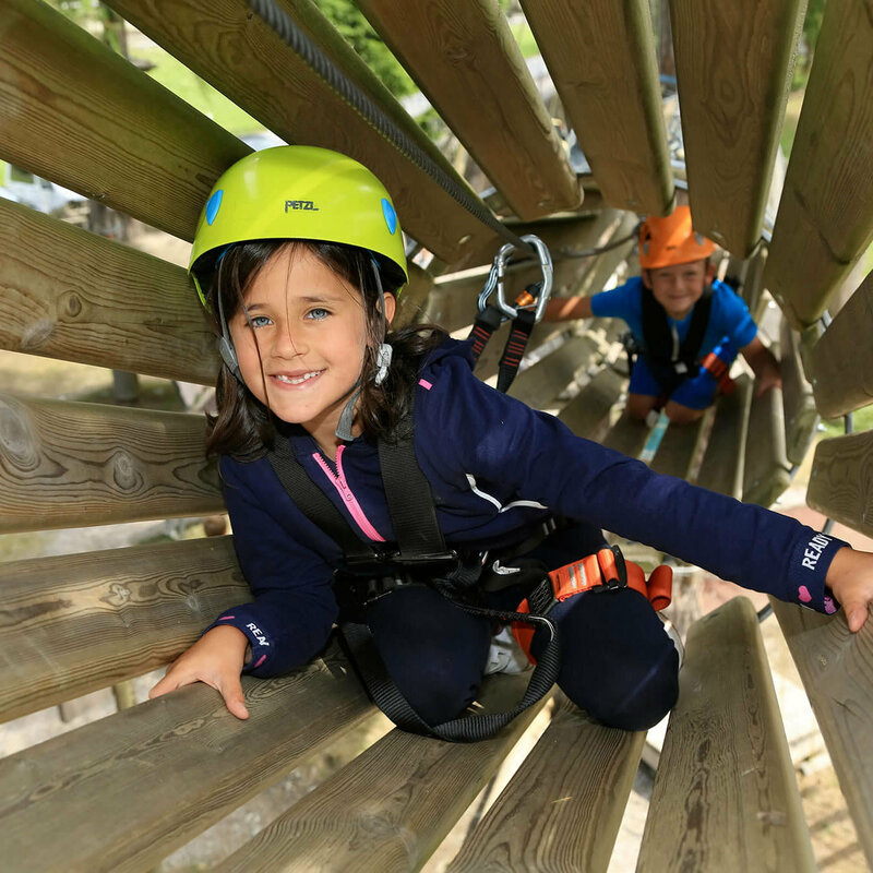 Aufnahme in ein hölzernes Rohr im Hochseilgarten in Sillian, wo zwei Kinder am Klettern sind.