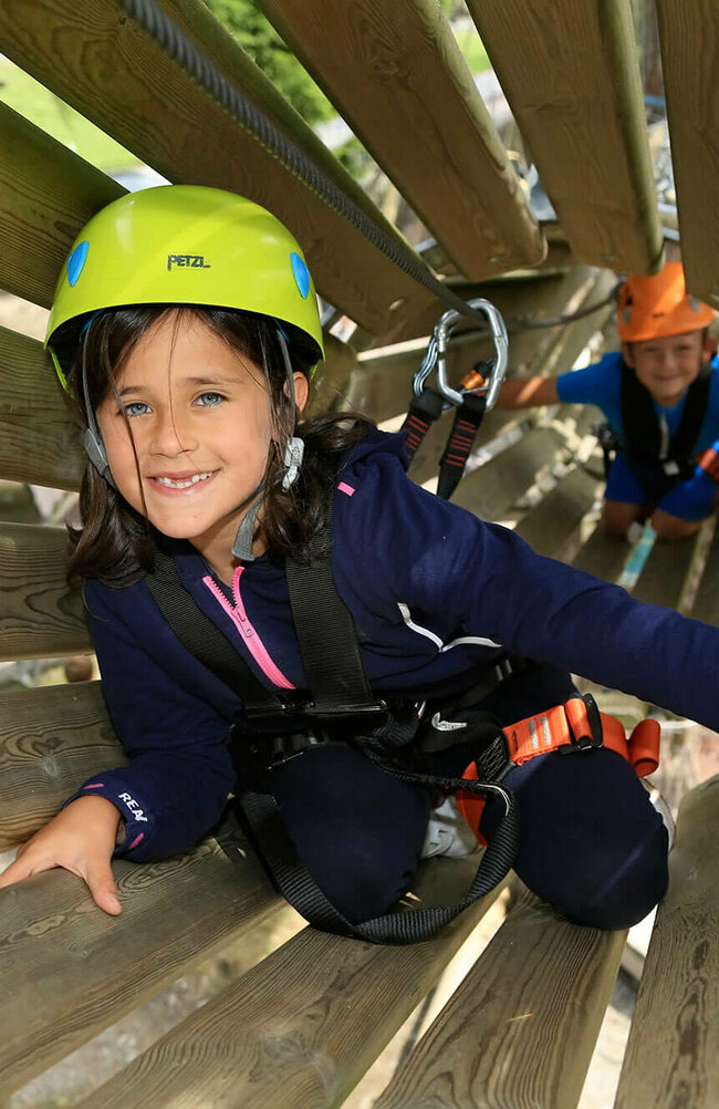 Aufnahme in ein hölzernes Rohr im Hochseilgarten in Sillian, wo zwei Kinder am Klettern sind.