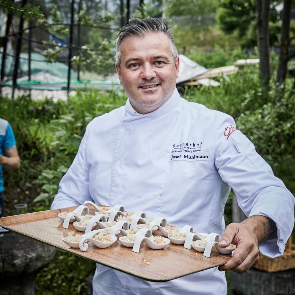 Josef Mühlmann vom Gannerhof präsentiert auf einem Tableau in seinen Hände die von ihm zubereiteten und angerichteten Gerichte auf weißen Löffeln.