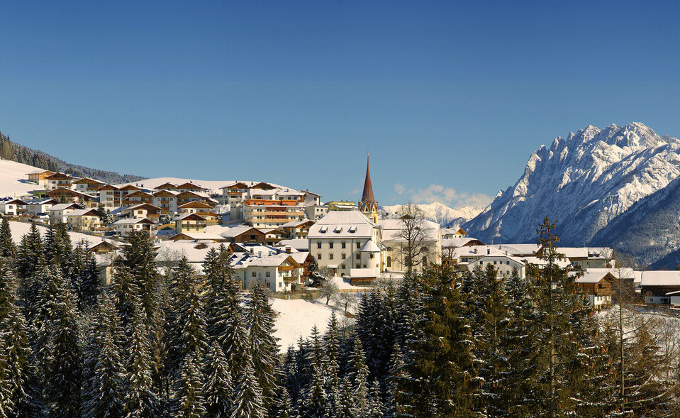 Blick auf Anras im Winter bei strahlend blauem Himmel mit den Lienzer Dolomiten im Hintergrund.