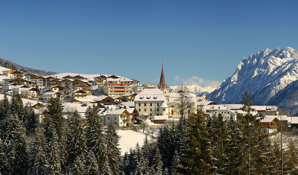 Blick auf Anras im Winter bei strahlend blauem Himmel mit den Lienzer Dolomiten im Hintergrund.