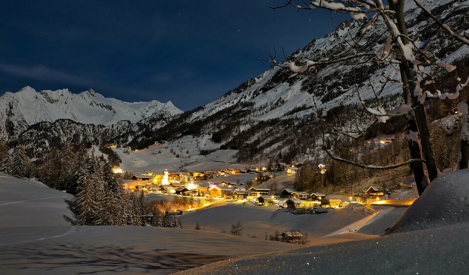 Das beleuchtete Dorf Prägraten am Großvenediger schneebedeckt in der Dämmerung.