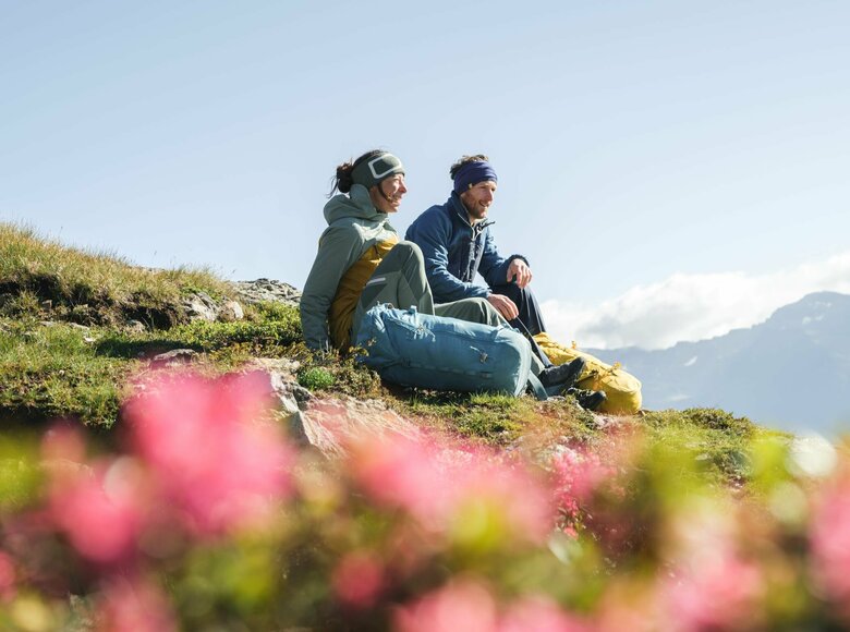 Ein Paar macht eine Pause auf einer Wiese mit Almrosen auf dem Weg zum Bösen Weibele zu einer Sonnenaufgangstour.