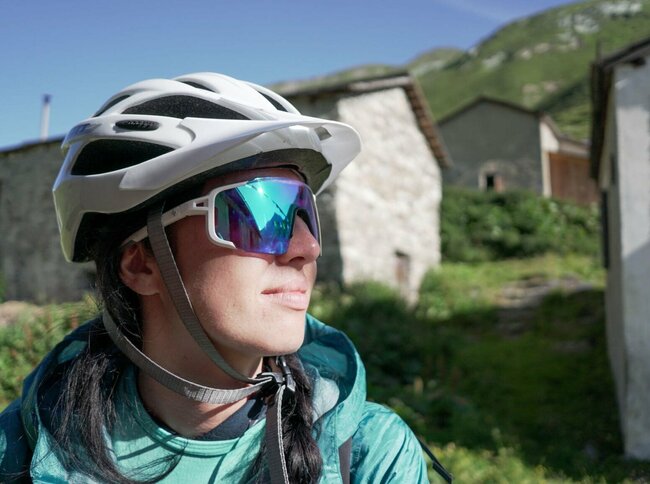 Eine Radfahrerin in Nahaufnahme - man sieht nur ihren Kopf mit Brille und Radhelm - im Hintergrund die Jagdhausalmen.