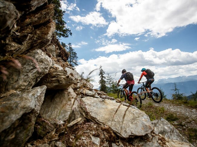 Zwei Radfahrer auf einem schmalen Weg auf der Compedalrunde im Kristeinertal. Im Vordergrund eine felsige Wand.