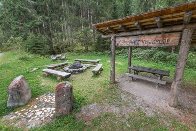Der Grillplatz Kohlgrube in Hopfgarten i. D.. Zu sehen ist ein mit Holz überdachter Grill der neben einer gemütlichen Sitzgelegenheit steht. Diese besteht aus vier Bänken die um einen Lagerfeuerplatz herum gestellt wurden.