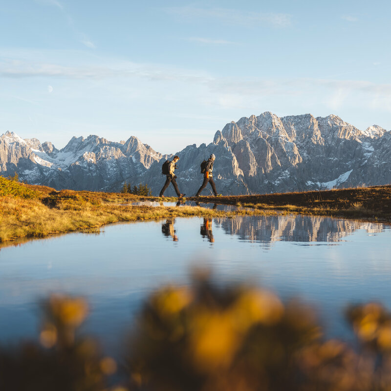 Zwei Personen spazieren am Bergsee am Hochstein bei traumhaftem Wetter mit Bergkulisse.
