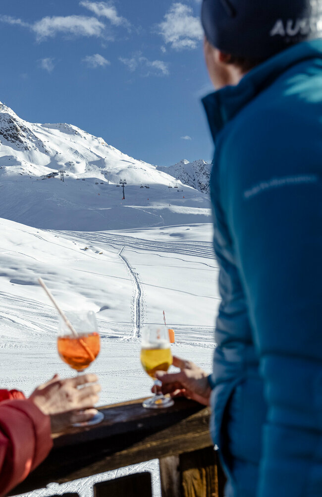 Skifahrer genießen ein Erfrischungsgetränk mit Blick auf die Pisten des Skizentrum St. Jakob i. D..