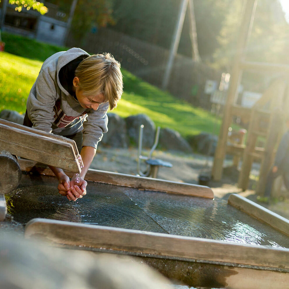 Ein Junge hält seine Hände ins Wasser bei einer Wasserstelle am Spielplatz in der Galitzenklamm.