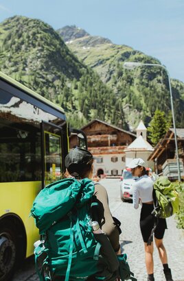 Zwei Wanderer steigen aus dem gelben Linienbus der ÖBB aus, im Hintergrund steht der traditionsreiche Gasthof „Matreier Tauernhaus“ in Matrei in Osttirol.