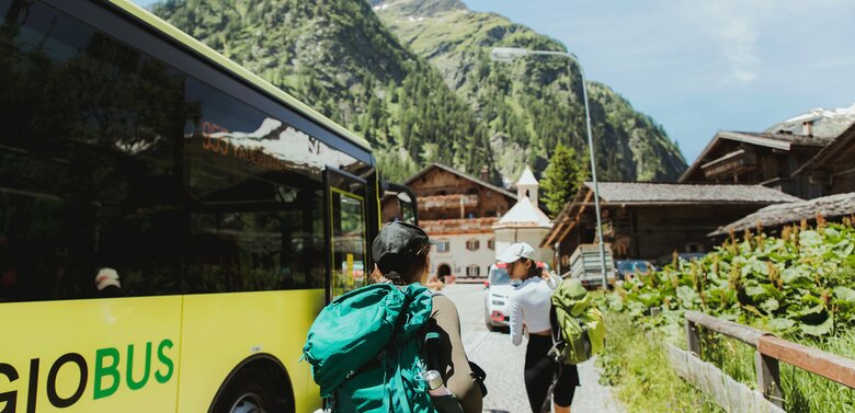 Zwei Wanderer steigen aus dem gelben Linienbus der ÖBB aus, im Hintergrund steht der traditionsreiche Gasthof „Matreier Tauernhaus“ in Matrei in Osttirol.