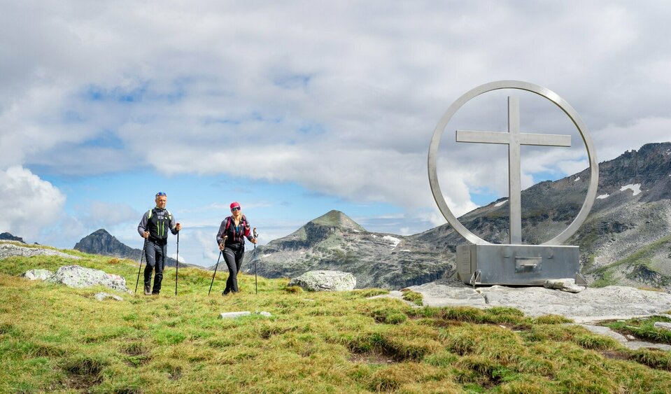 Weitwandern auf der Glocknerkrone in Osttirol, Etappe 2: Wanderer am Gipfelkreuz Spinewitrol mit Blick nach Norden auf den Medelzkopf nahe Kals am Großglockner.