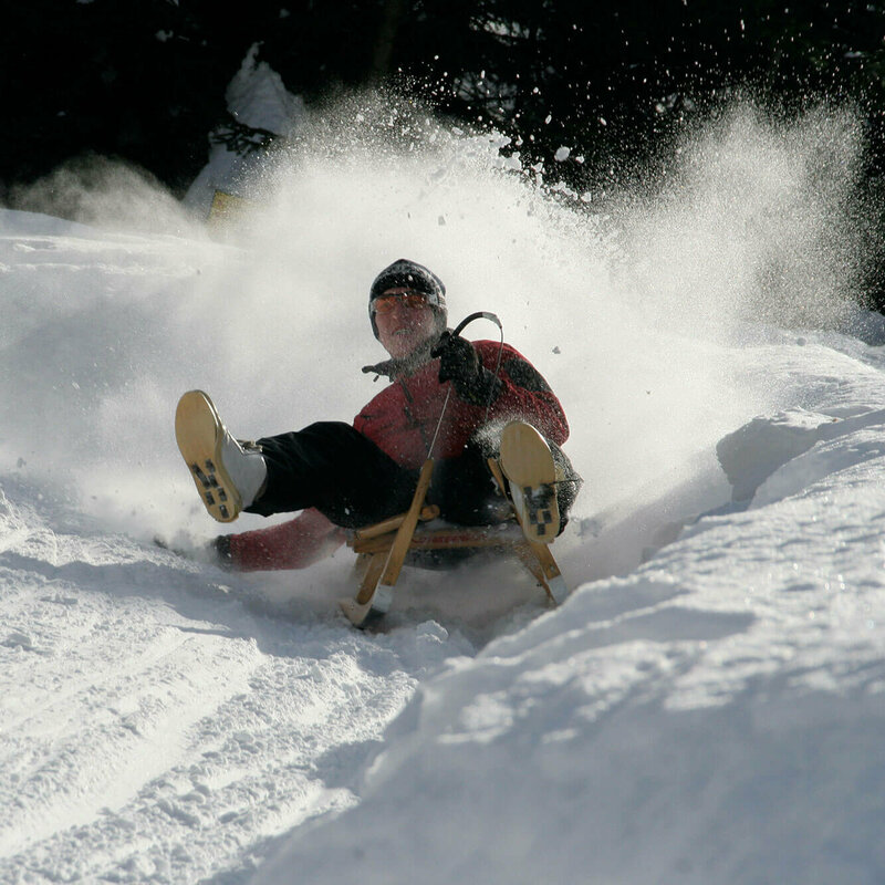 Da staubt der Pulverschnee, als der Rodler die Kurve einer Rodelbahn nimmt. Ein natürlcher Schneewall begrenzt die Bahn.