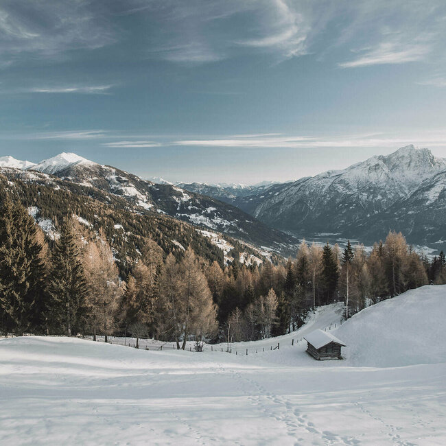 Spuren im Schnee an einem Berg mit Aussicht auf den verschneiten Lienzer Talboden.