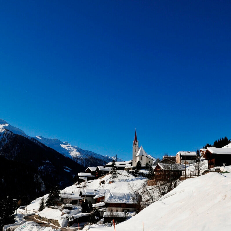 Blick auf das winterliche St. Veit im Defereggental mit verschneiten Dächern bei Kaiserwetter.
