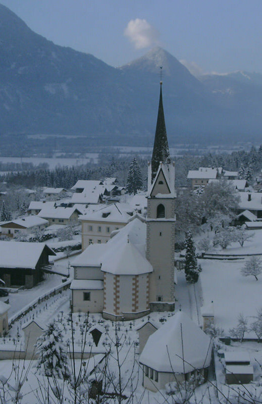 Die Kirche in Nikolsdorf liegt im Schnee an einem trüben Wintertag.