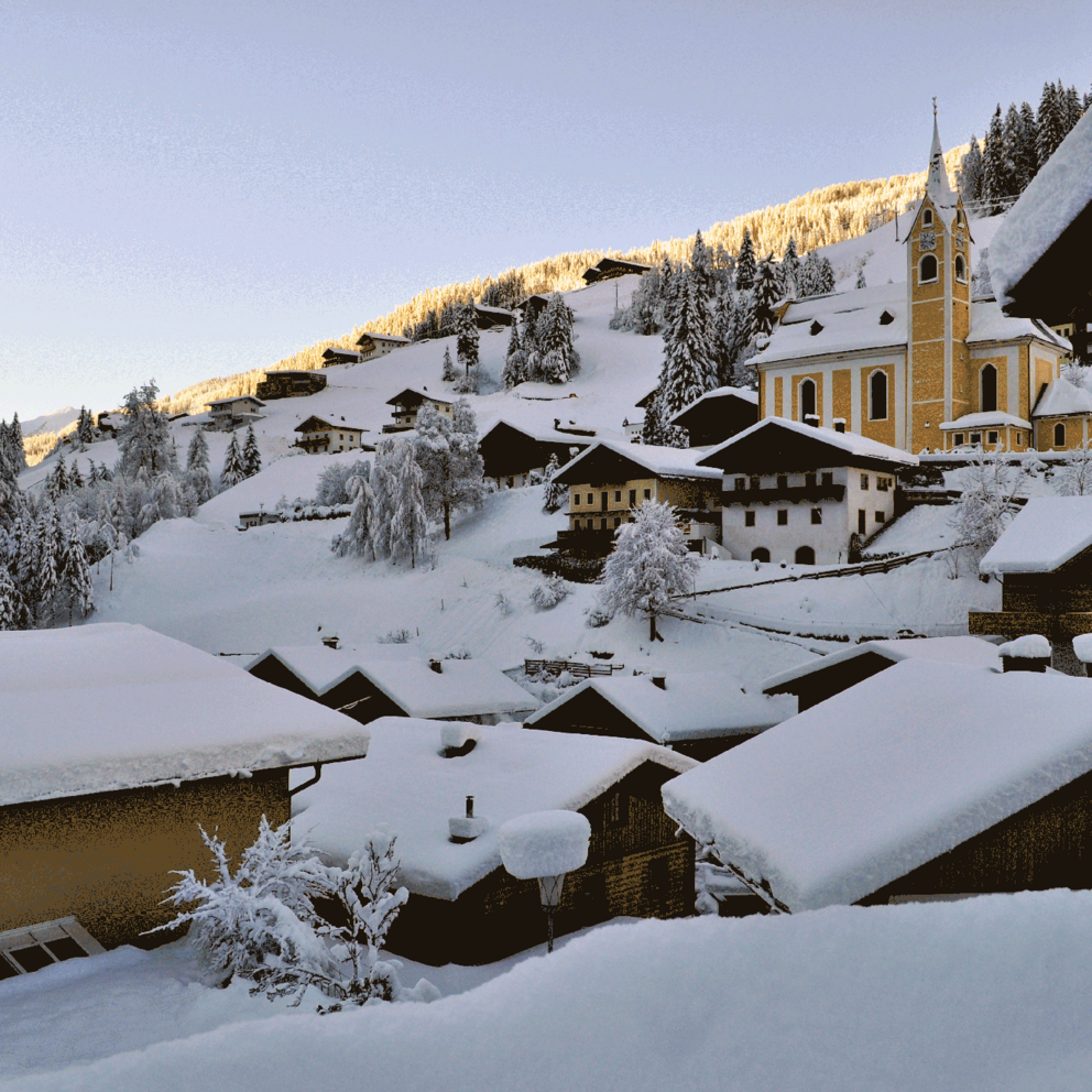 Ausservillgraten mit schneebedeckten Dächern und der Kirche im Winter.