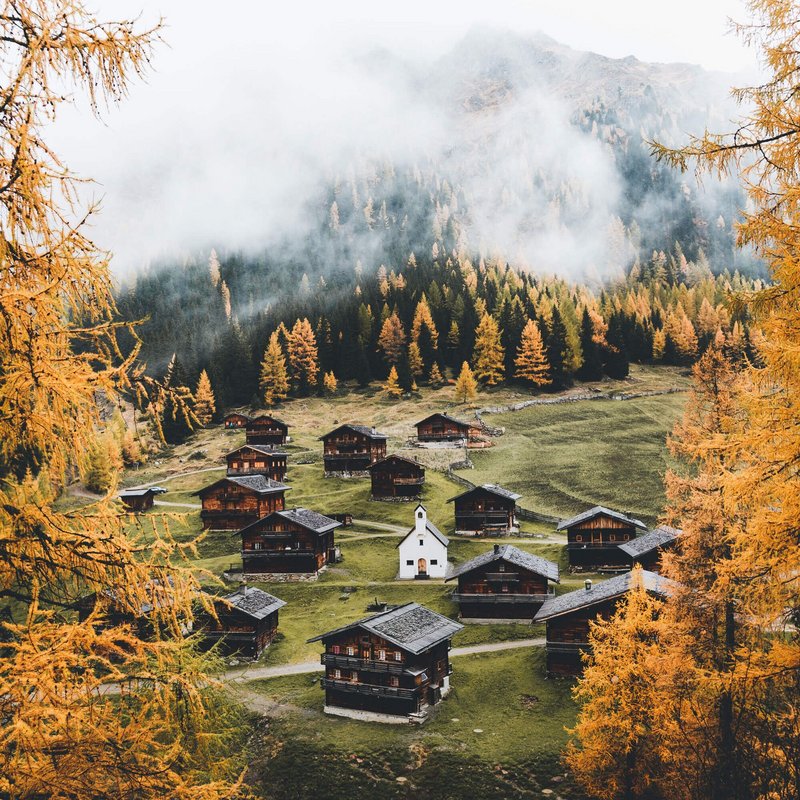 Die Hüttenansammlung mit kleiner Kapelle in der Mitte der Oberstalleralm in herbstlicher Umgebung mit verfärbten Wäldern.